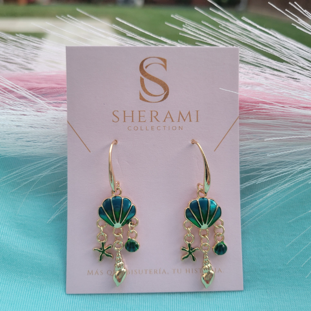 Par de pendientes playeros en tonos dorados, azul y verdes en una tarjeta de Sherami Collection con un fondo decorativo.