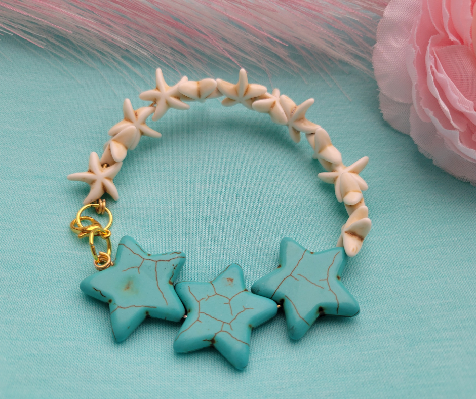 Pulsera de estrellas de mar crema y turquesa de Sherami Collection sobre un fondo azul