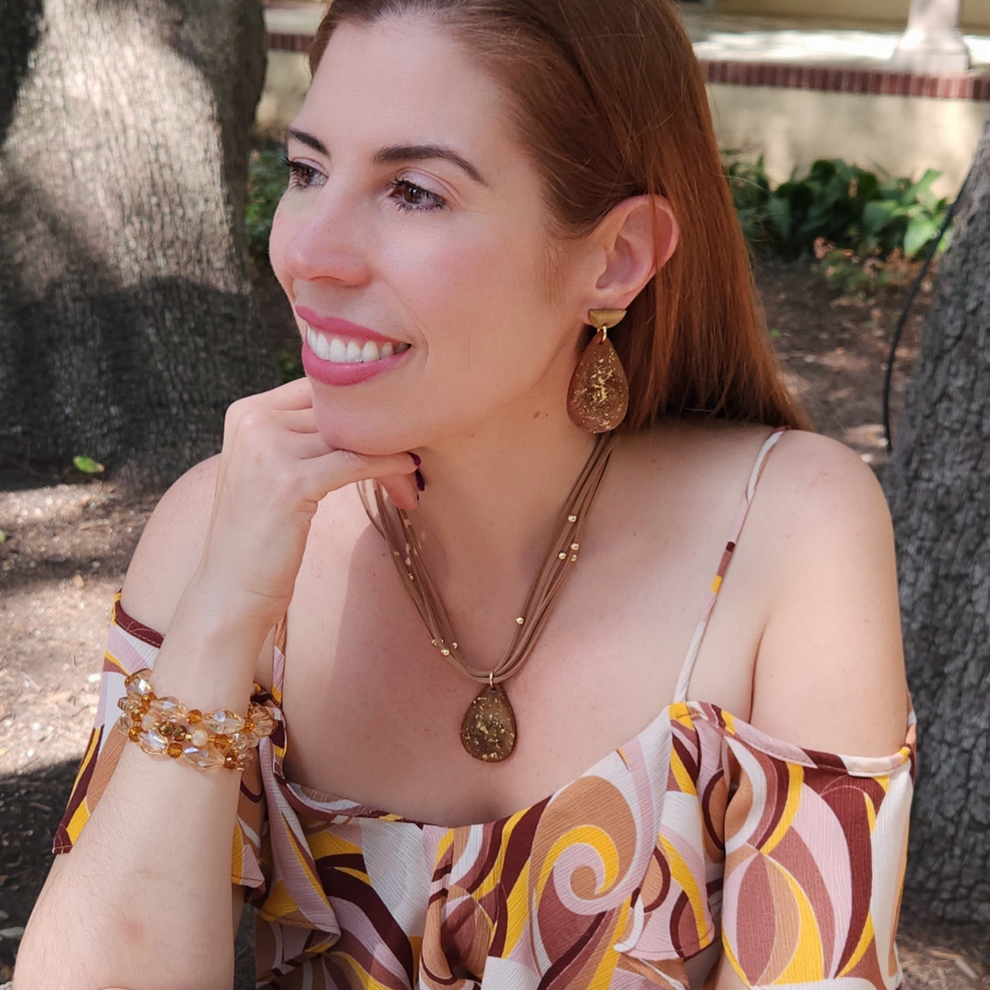 Woman wearing a patterned dress and gold and brown jewelry outdoors Sherami Collection Fall Collection