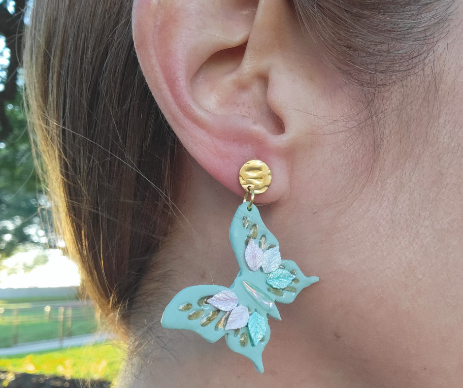 Aretes verde claro en forma de mariposa con detalles primaverales y gancho dorado.