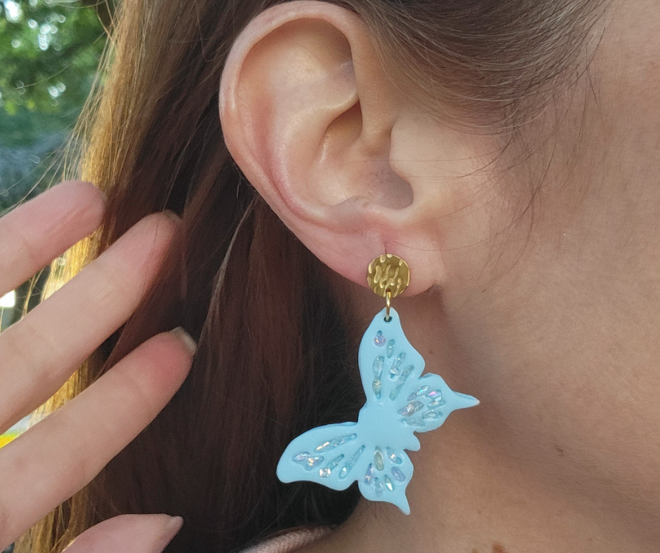 Aretes azul en forma de mariposa con detalles primaverales y gancho dorado.