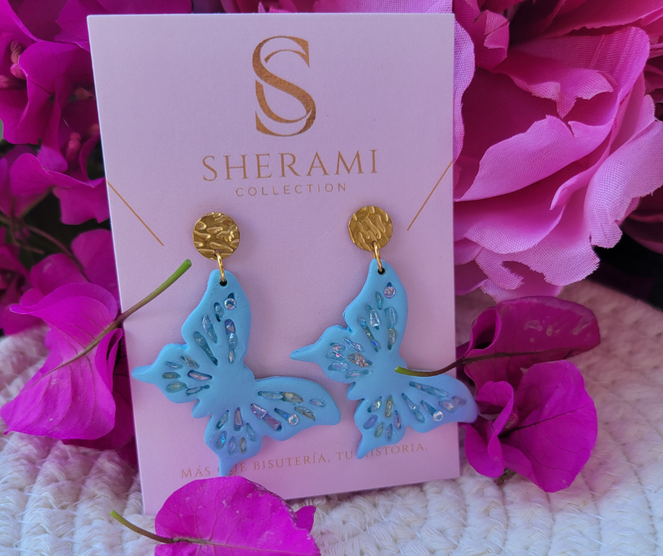 Aretes azul en forma de mariposa con detalles primaverales y gancho dorado.