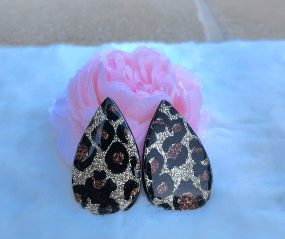 Aretes Sherami Collection con estampado animal de cheetah con destellos dorados sobre fondo rosa y blanco