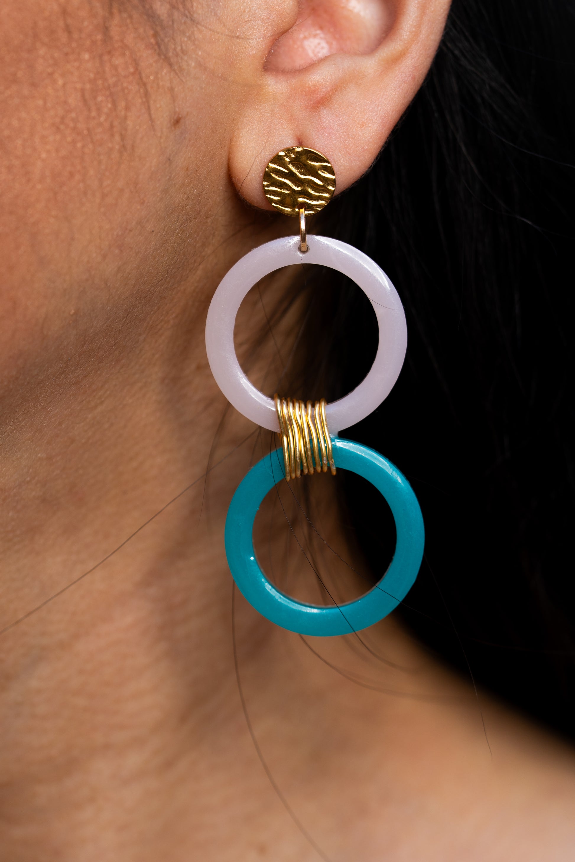 Primer plano de un pendiente de Sherami Collection  con un diseño circular azul y blanco  en una oreja.