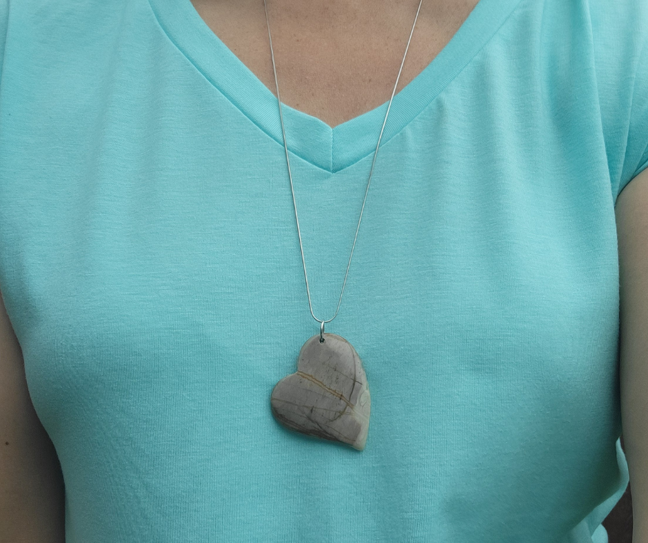 Person wearing a turquoise shirt with a necklace featuring a stone pendant.
