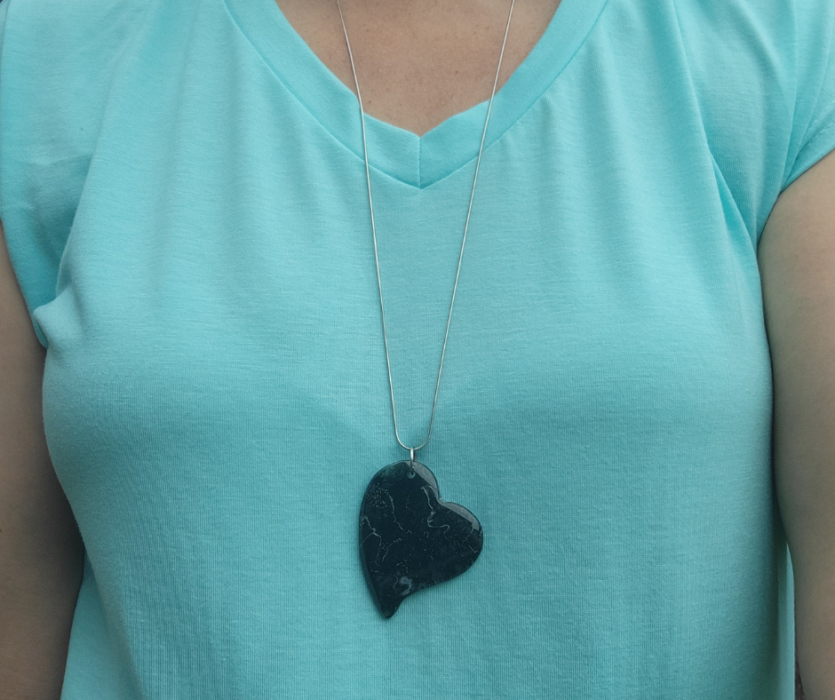 Person wearing a turquoise shirt with a necklace featuring a black heart pendant.