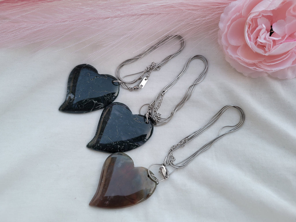 Collar largo con dije grande en forma de corazón sobre una superficie suave.