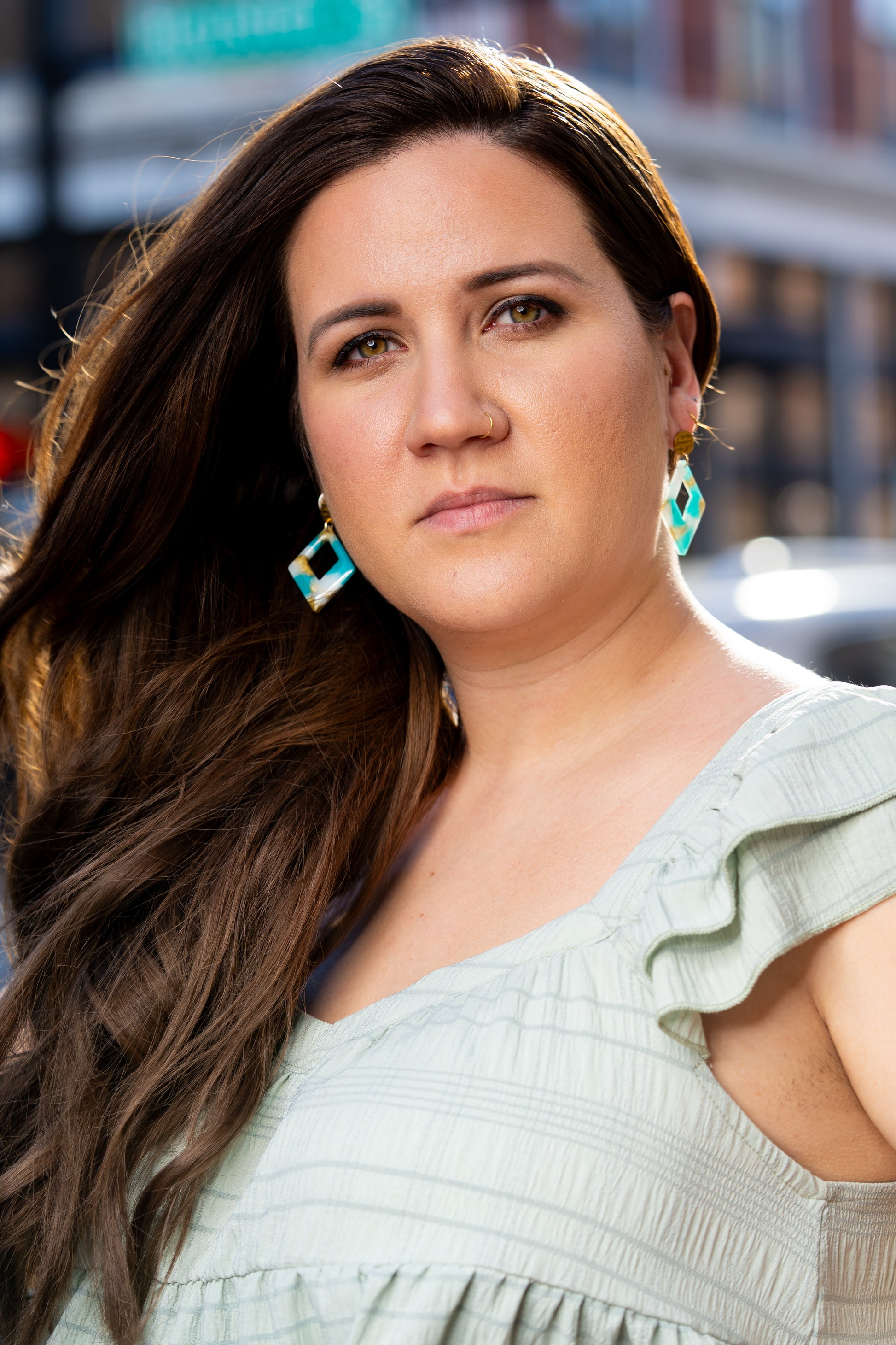 Woman with long brown hair wearing a light green top and a pair of Sherami Collection earrings, looking to the side.