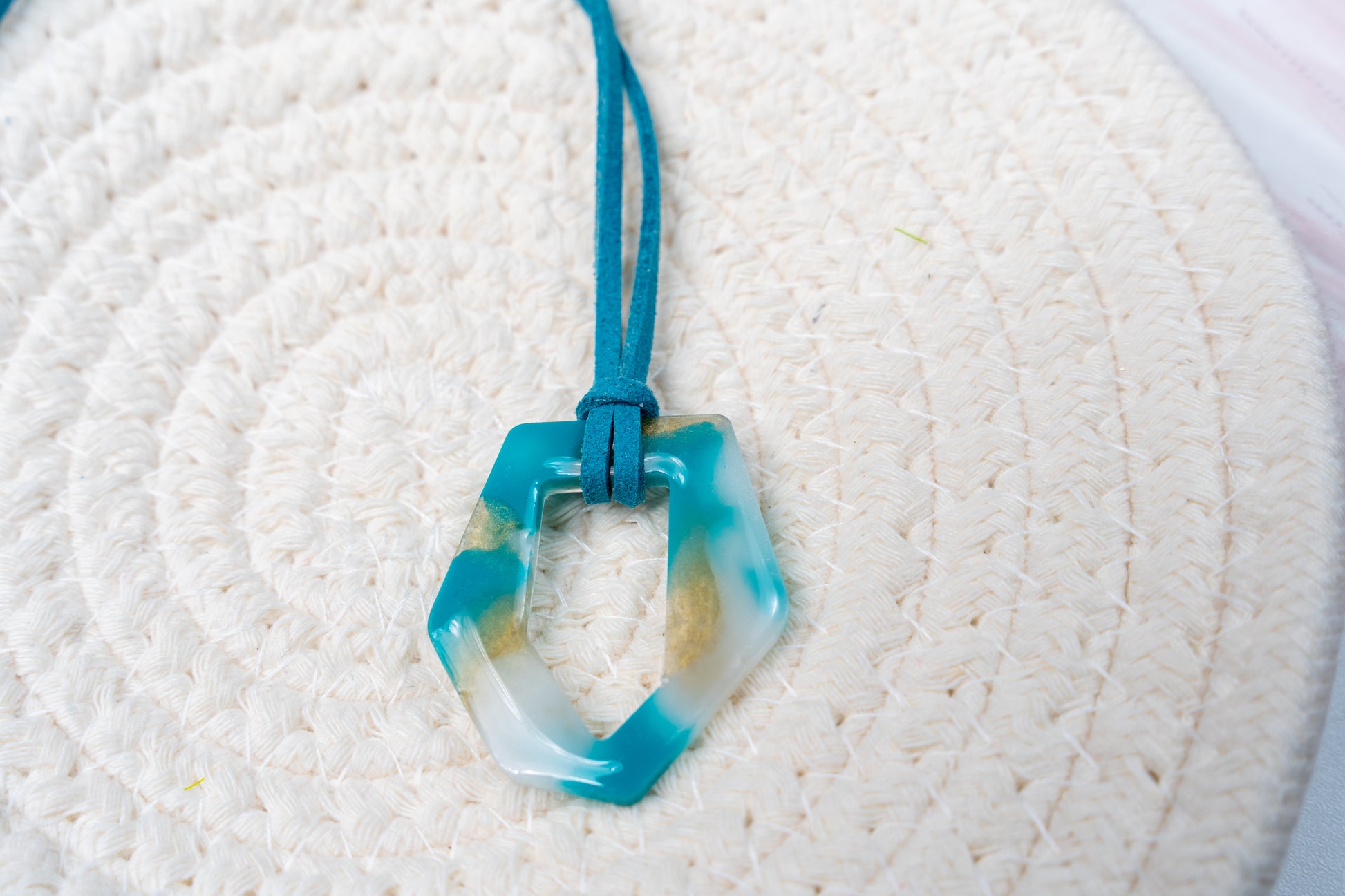 Collar con colgante azul, blanco y dorado de la marca Sherami Collection sobre una superficie tejida blanca.