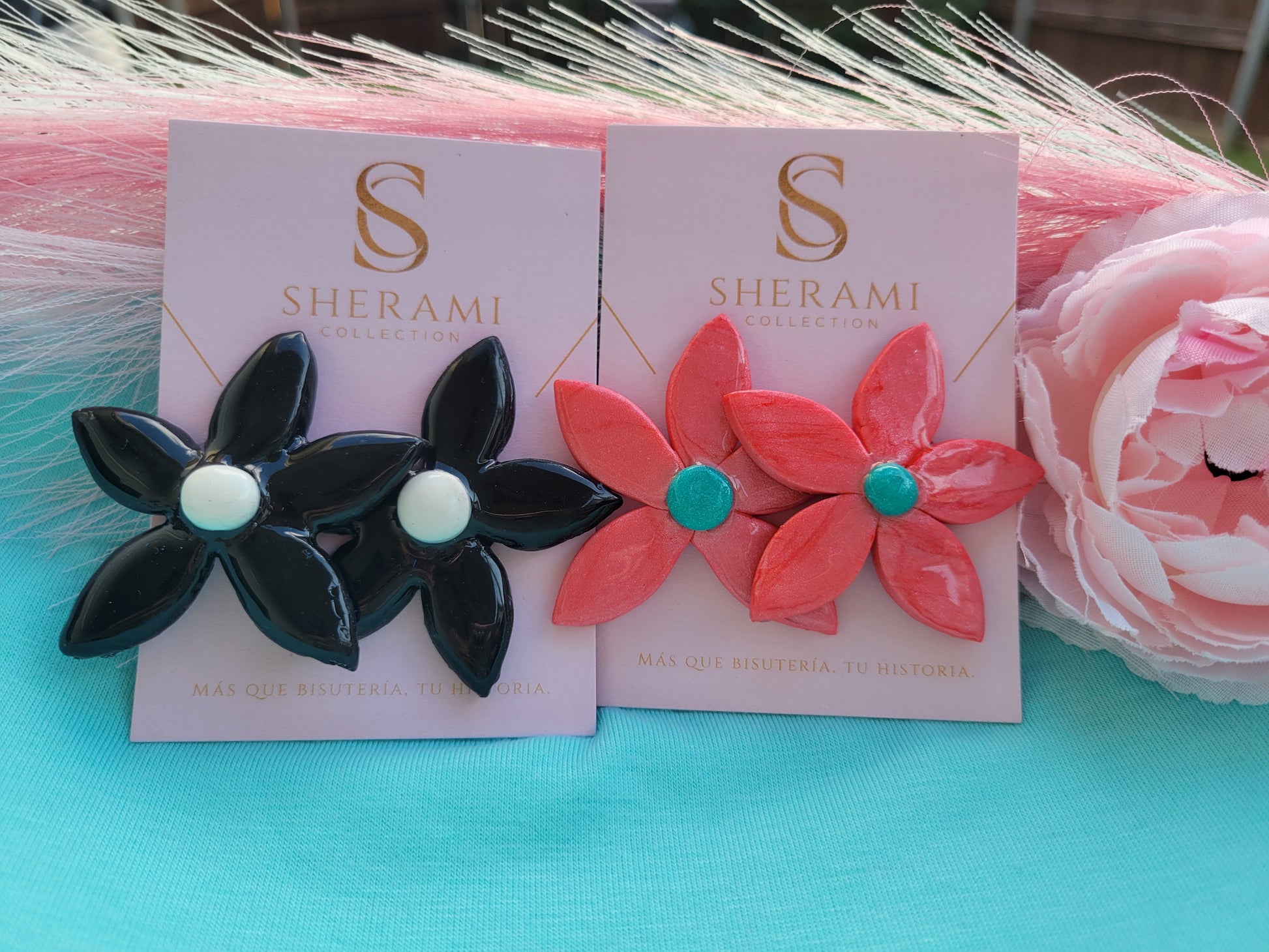 Aretes rtsanales de arcilla en forma de flore en rosa y en negro sobe la tarjeta de Sherami Collection