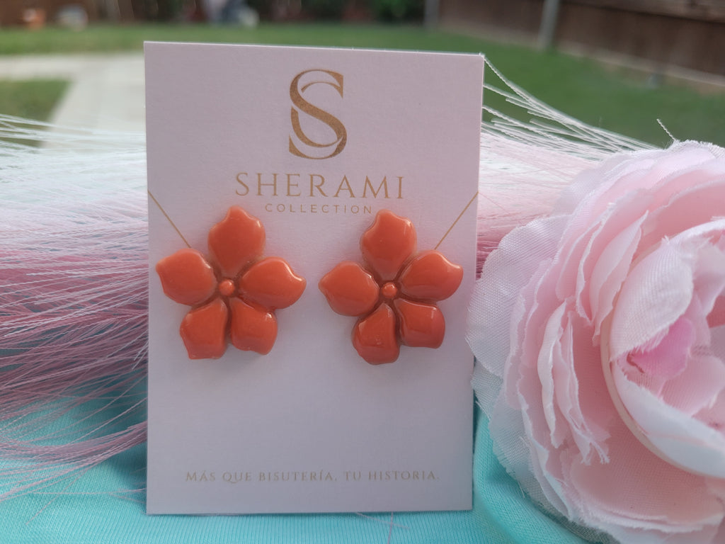 Orange flower-shaped earrings on a Sherami Collection branded card with a pink flower in the background.
