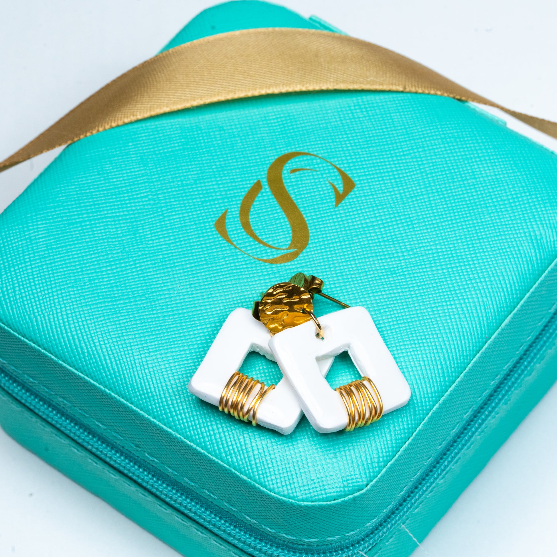 Turquoise jewelry case with gold ribbon and white Invicta earrings from Sherami Collection on a white background