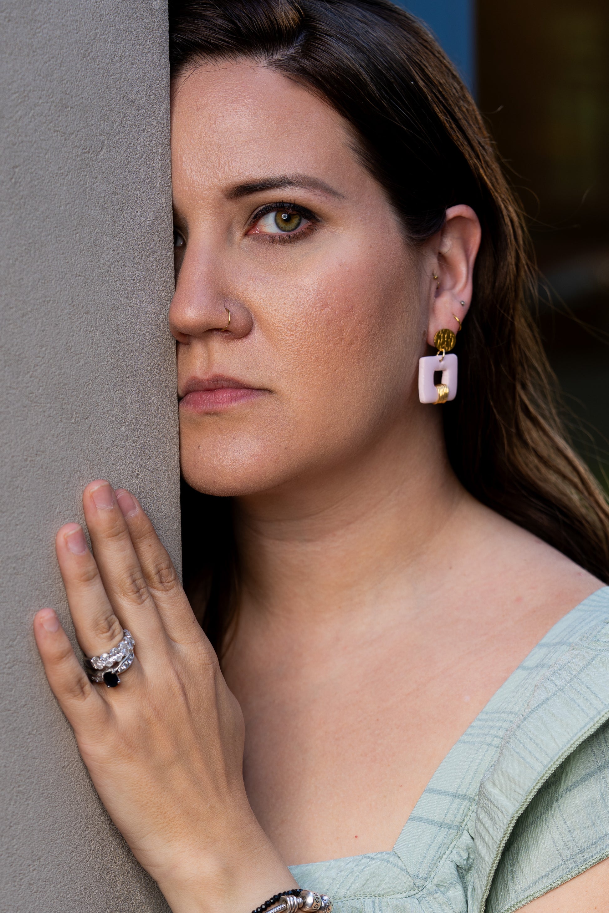 Woman with Invicta earrings from Sherami Collection, looking over a gray surface