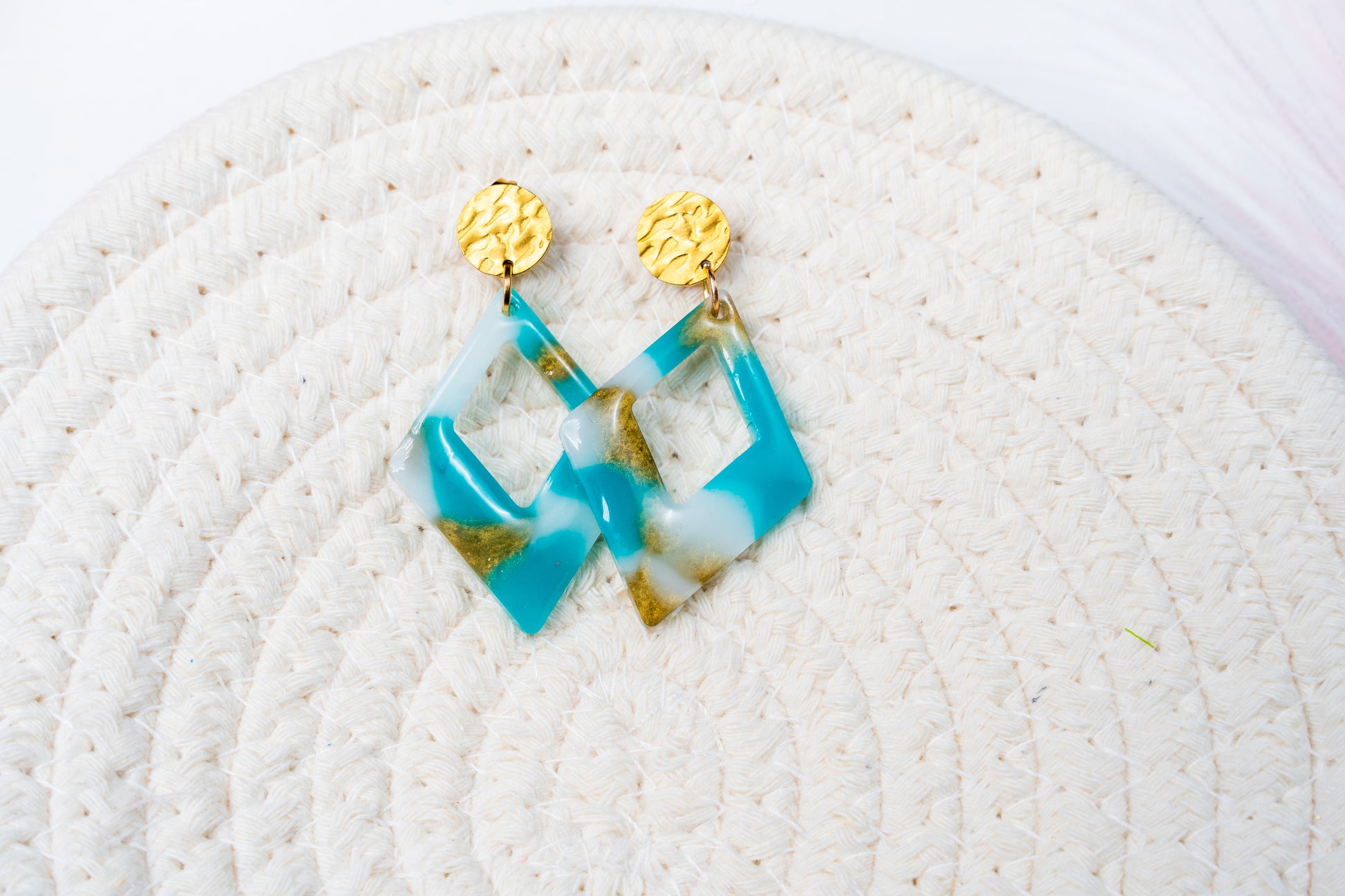 Pair of turquoise, white, and gold earrings from Sherami Collection  on a textured white surface