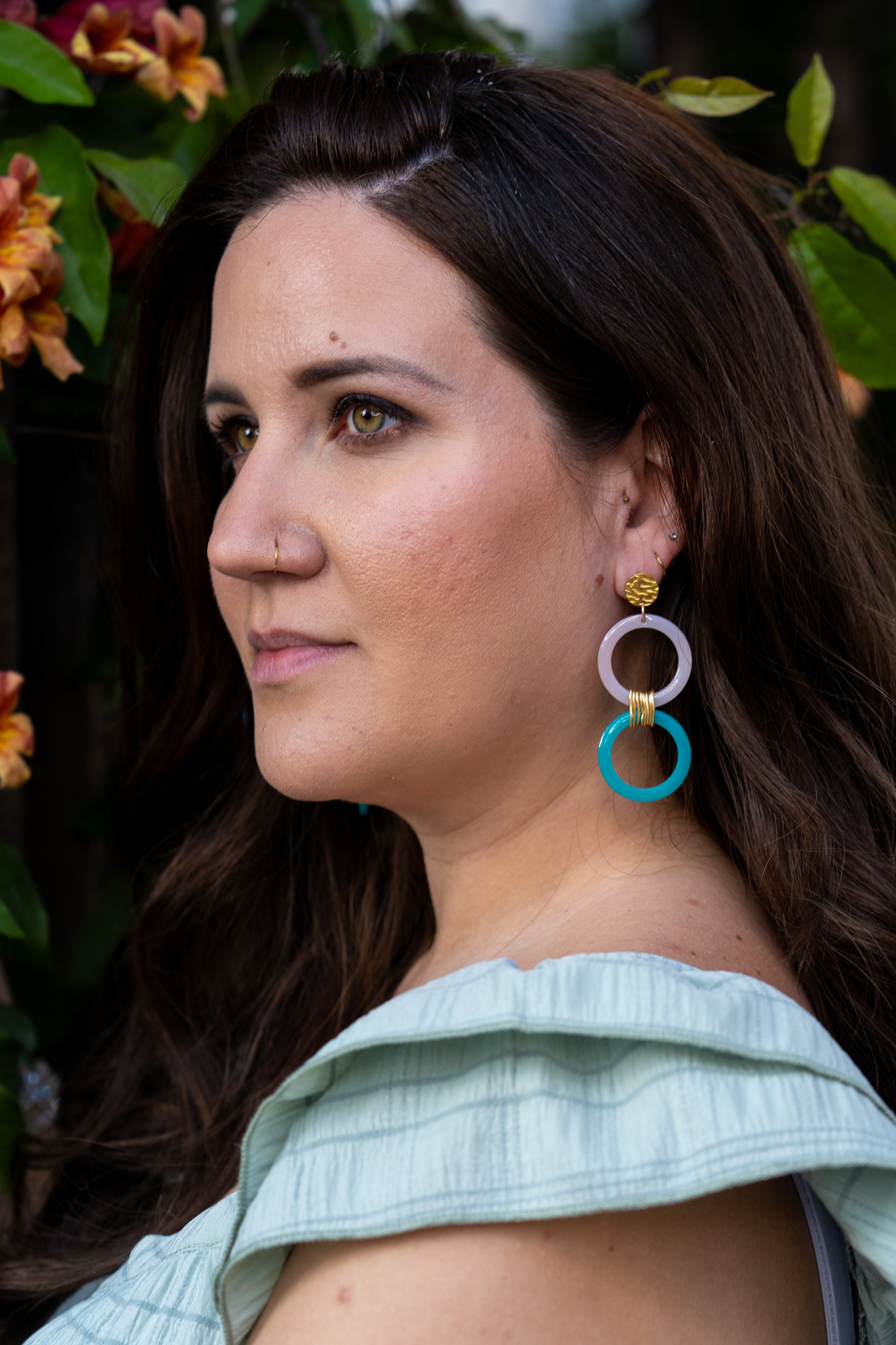Mujer con pendientes modelo  Iconica de Sherami Collection con fondo floral.