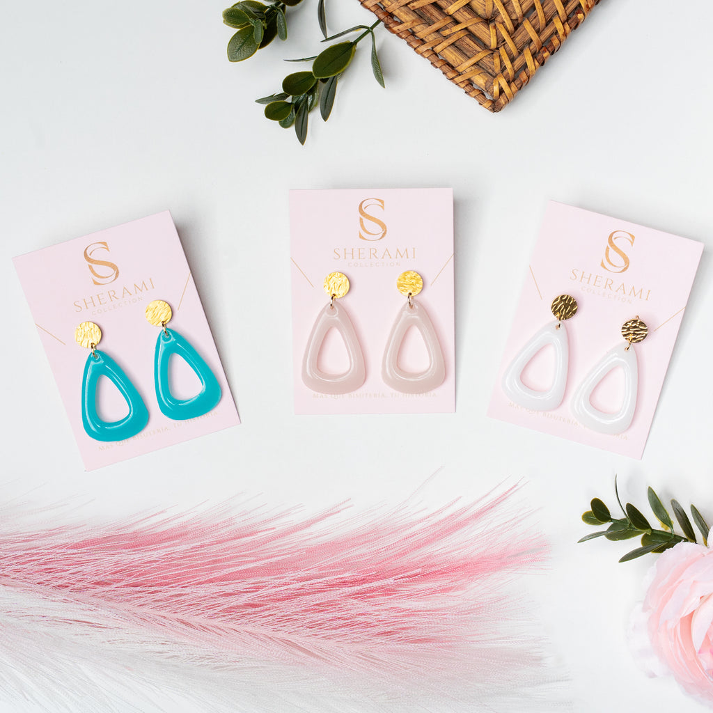 Three pairs of earrings on branded Sherami Collection cards with a decorative background