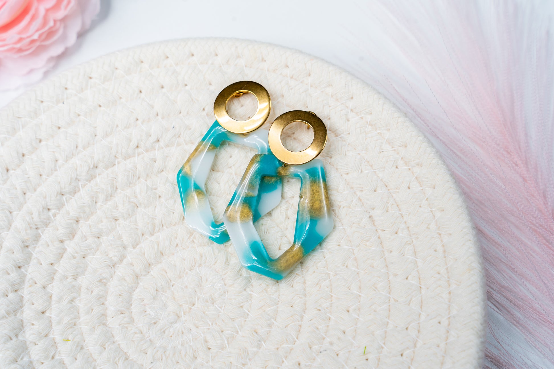 Par de pendientes e Sherami Collection  con diseño dorado, blanco y azul sobre una superficie blanca.