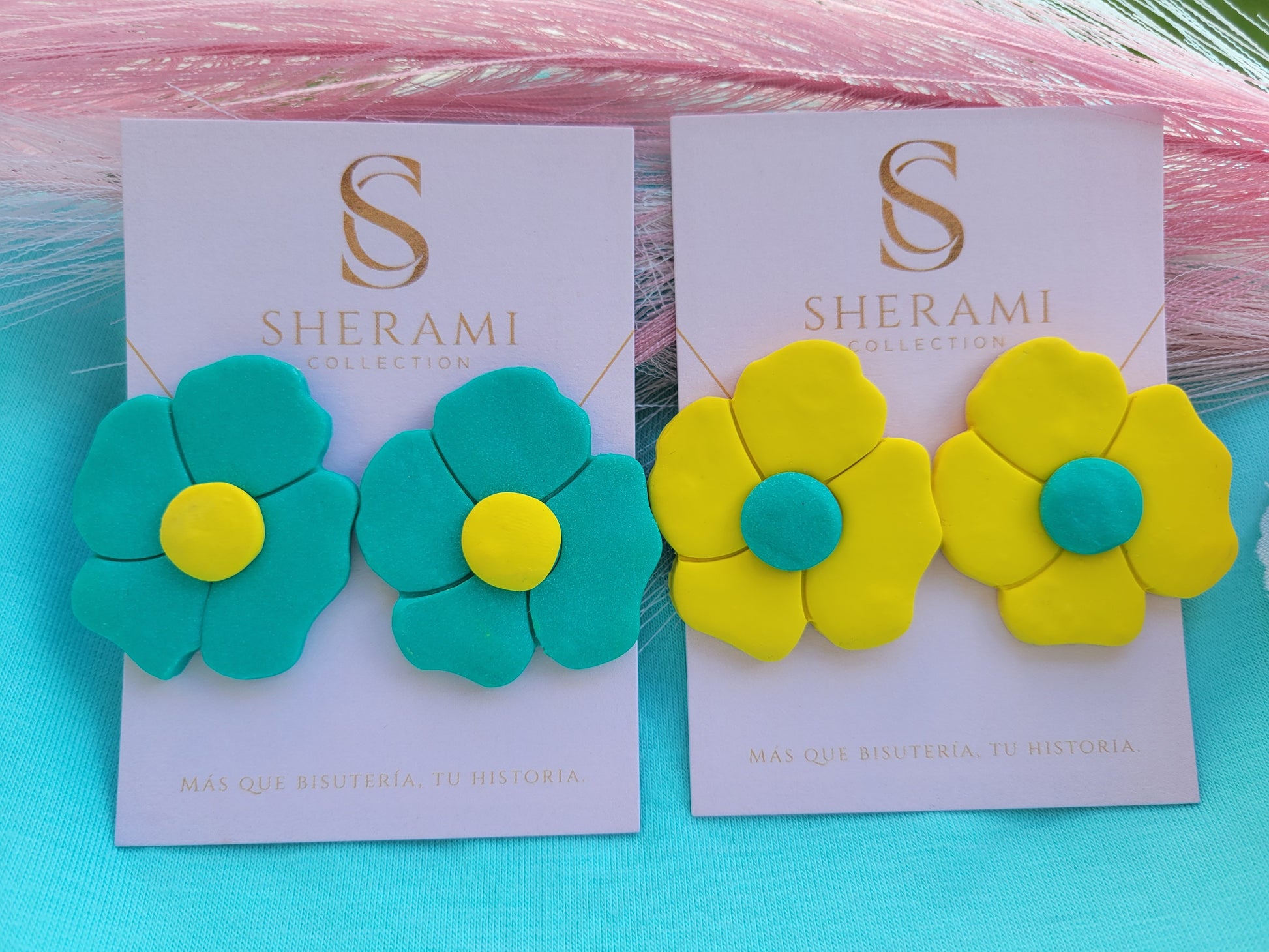Dos pares de pendientes con forma de flor en tarjetas de la marca Sherami Collection sobre un fondo rosa.