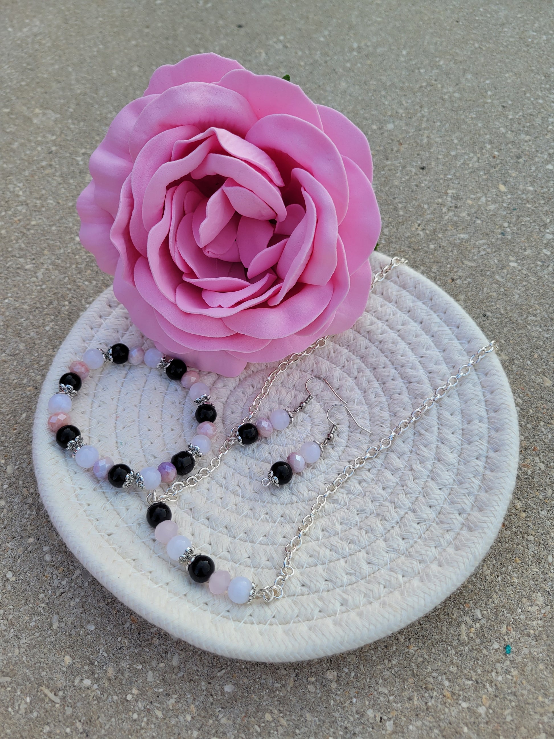 Se muestra set de collar, pulsera y aretes de cuentas de cristal rosa, negras y blancas.