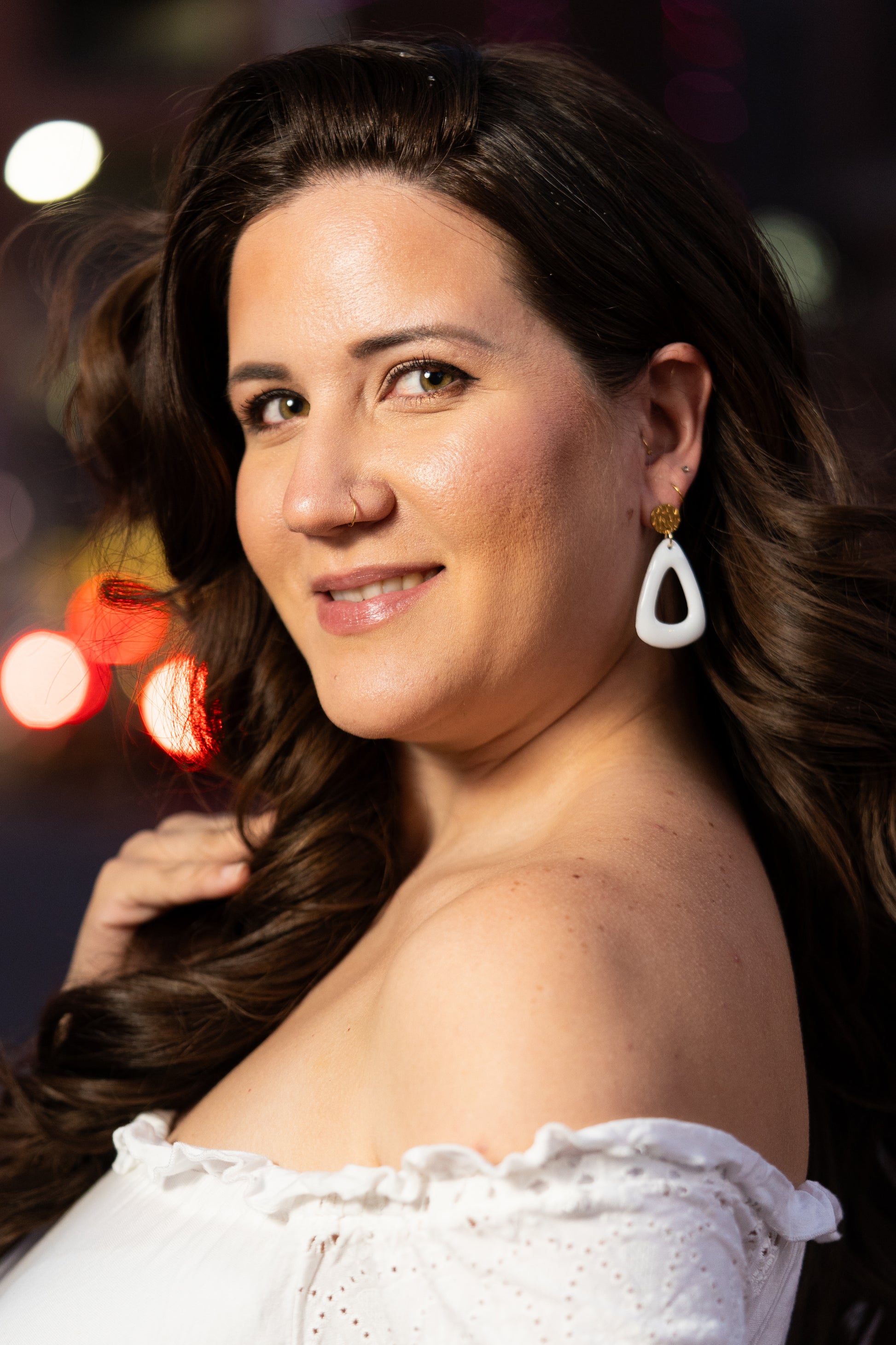 Woman wearing white Sherami Collection earrings with blurred lights in the background