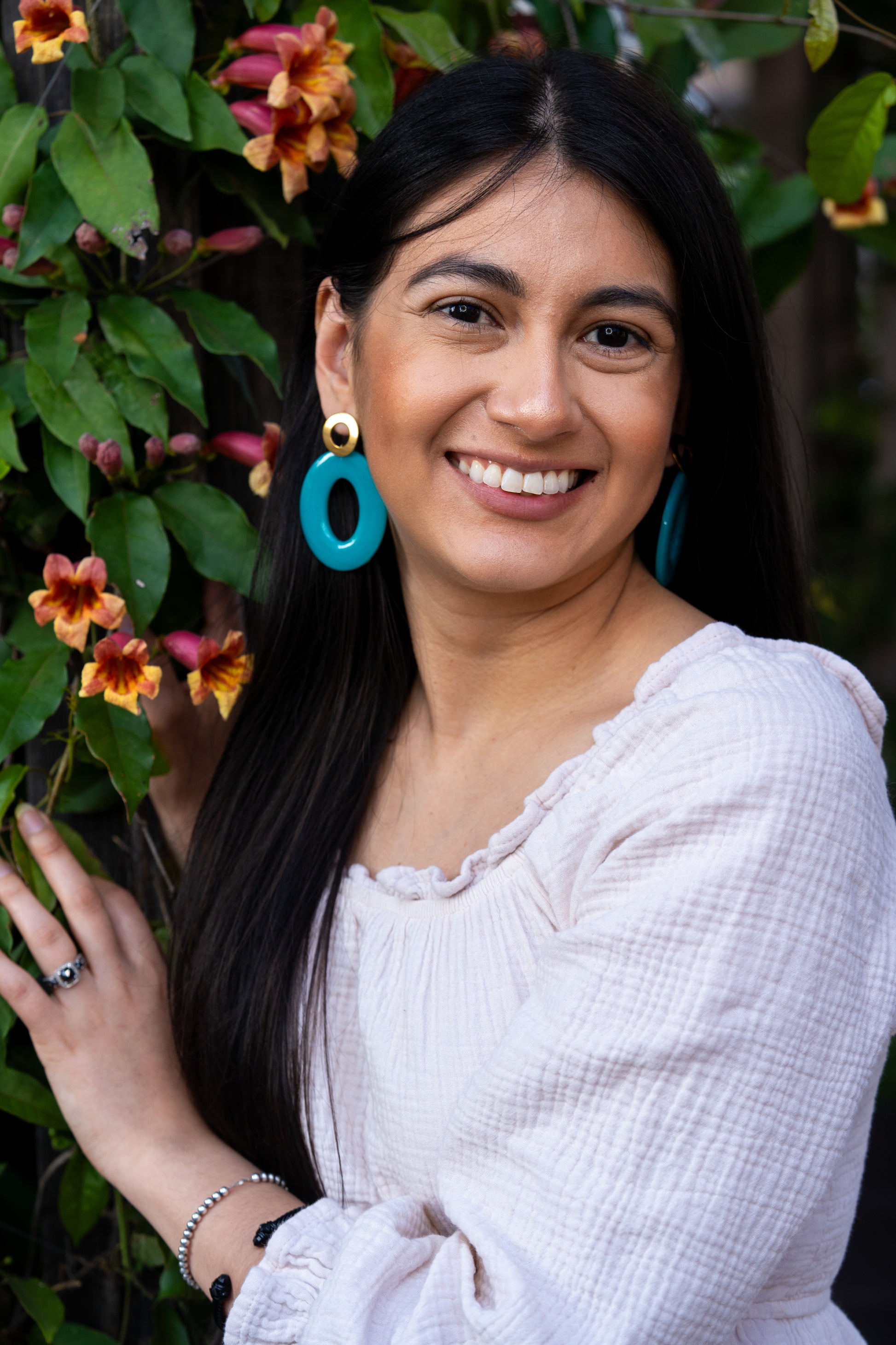 Woman with a blue  Sherami Collection earring lying among flowers and greenery