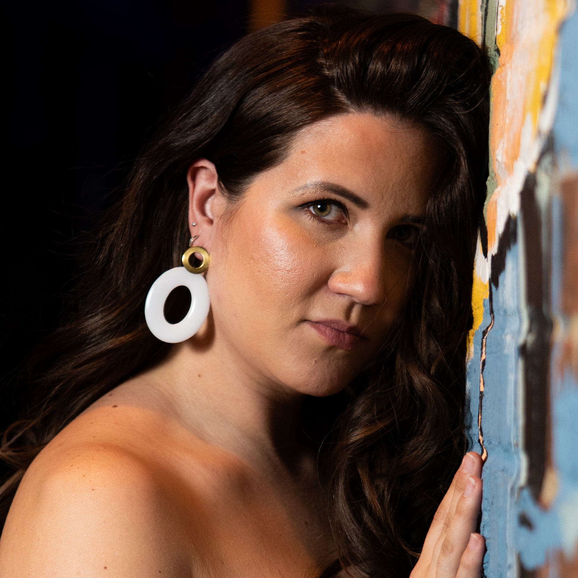 Woman lying on a colorful wall with Sherami Collection earrings on display