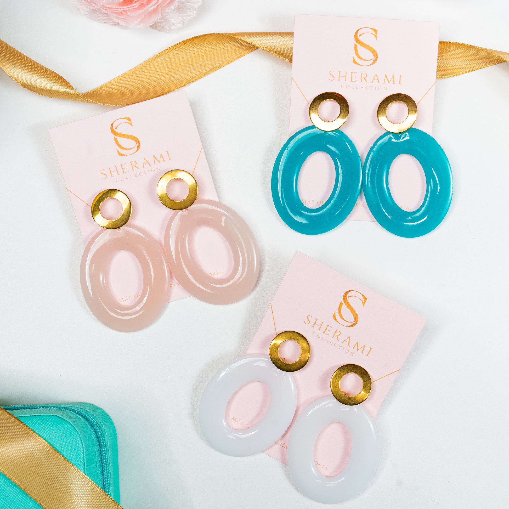 3 pair of earrings  with gold accents on a pink Sherami Collection  card, surrounded by decorative ribbons and a box.