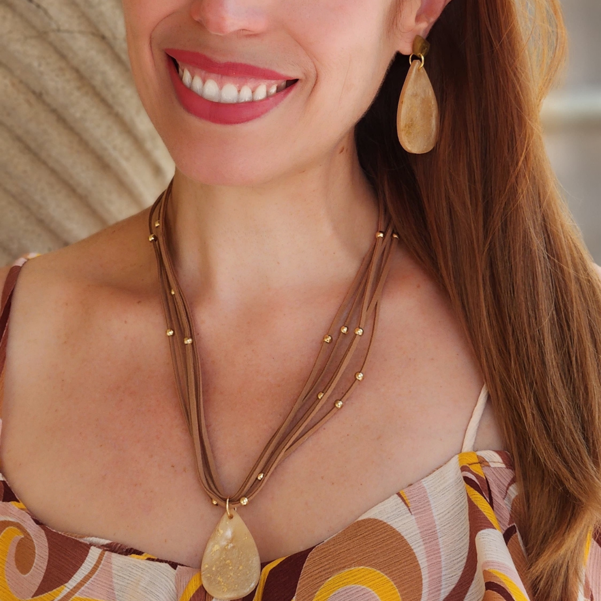 Mujer vistiendo conjunto de aretes y collar artesal en colores crema , marrón y dorados de Sherami Collection.