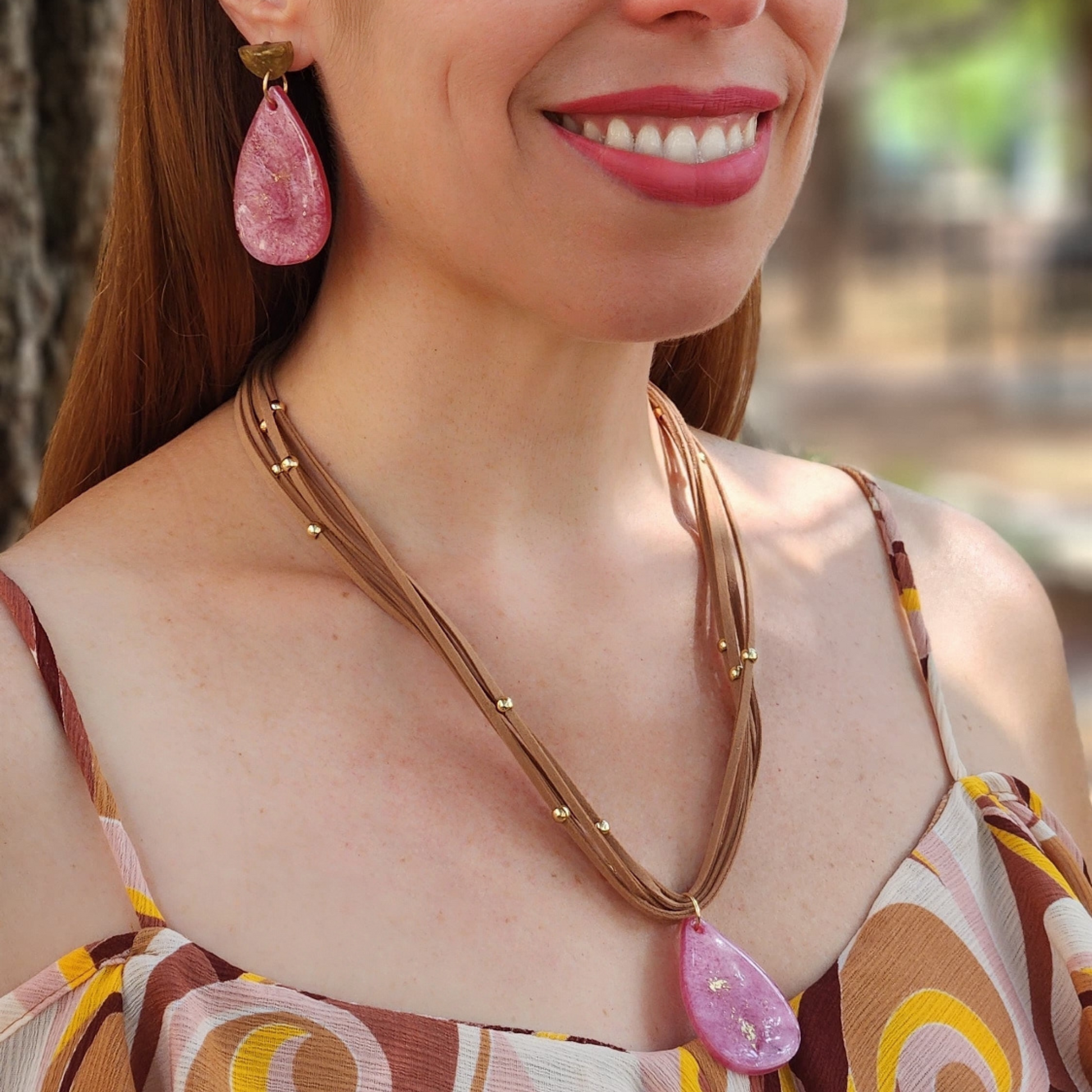 Mujer vistiendo un conjuto de aretes y collar artesanal en rosa y marrón de Sherami Collection