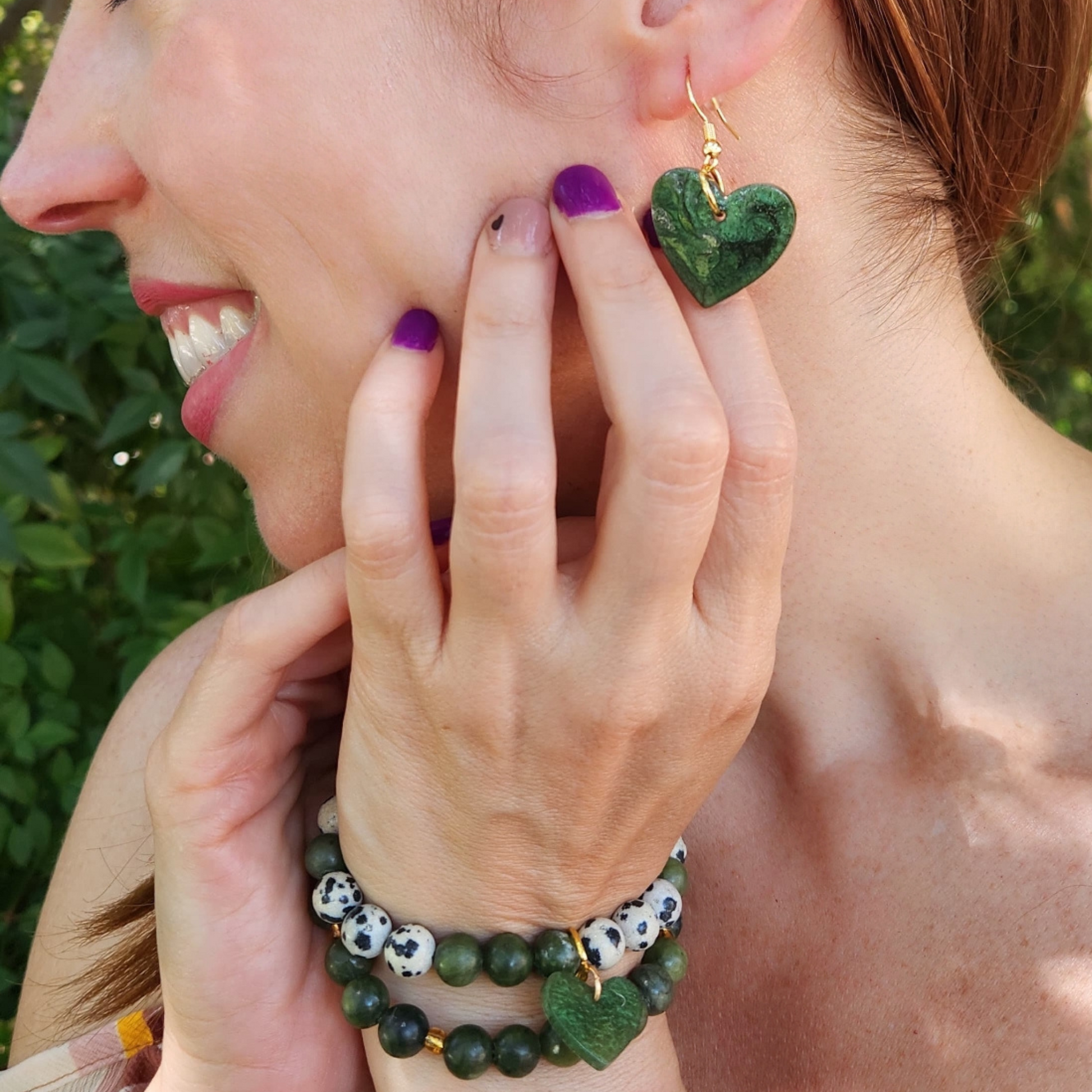 Woman wearing green heart-shaped earrings and bracelets outdoors from Sherami Collection