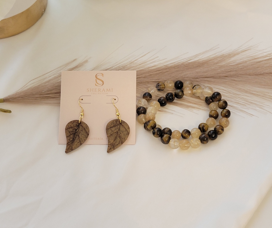 Se muestra un par de aretes en forma de hoja marró junto a dos pulseras de cuentas marrones y amarillas.