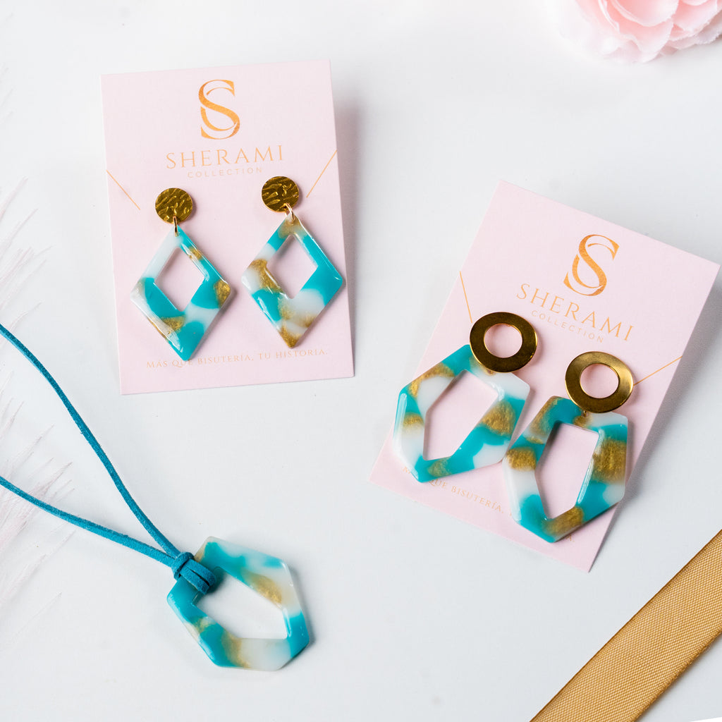 Turquoise and gold earrings on pink Sherami Collection cards with a necklace.