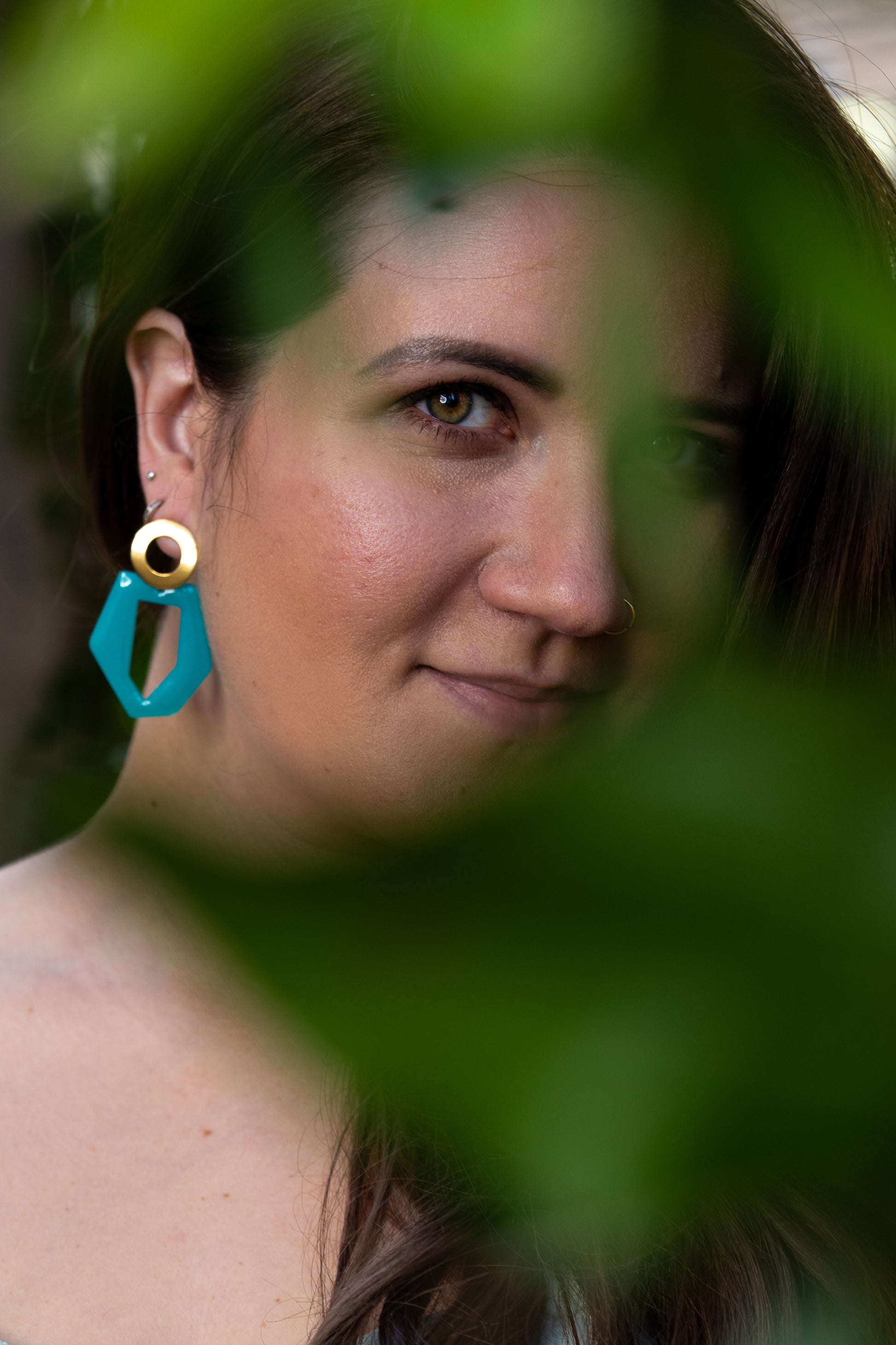 Person wearing Sherami Collection blue earrings, surrounded by green leaves