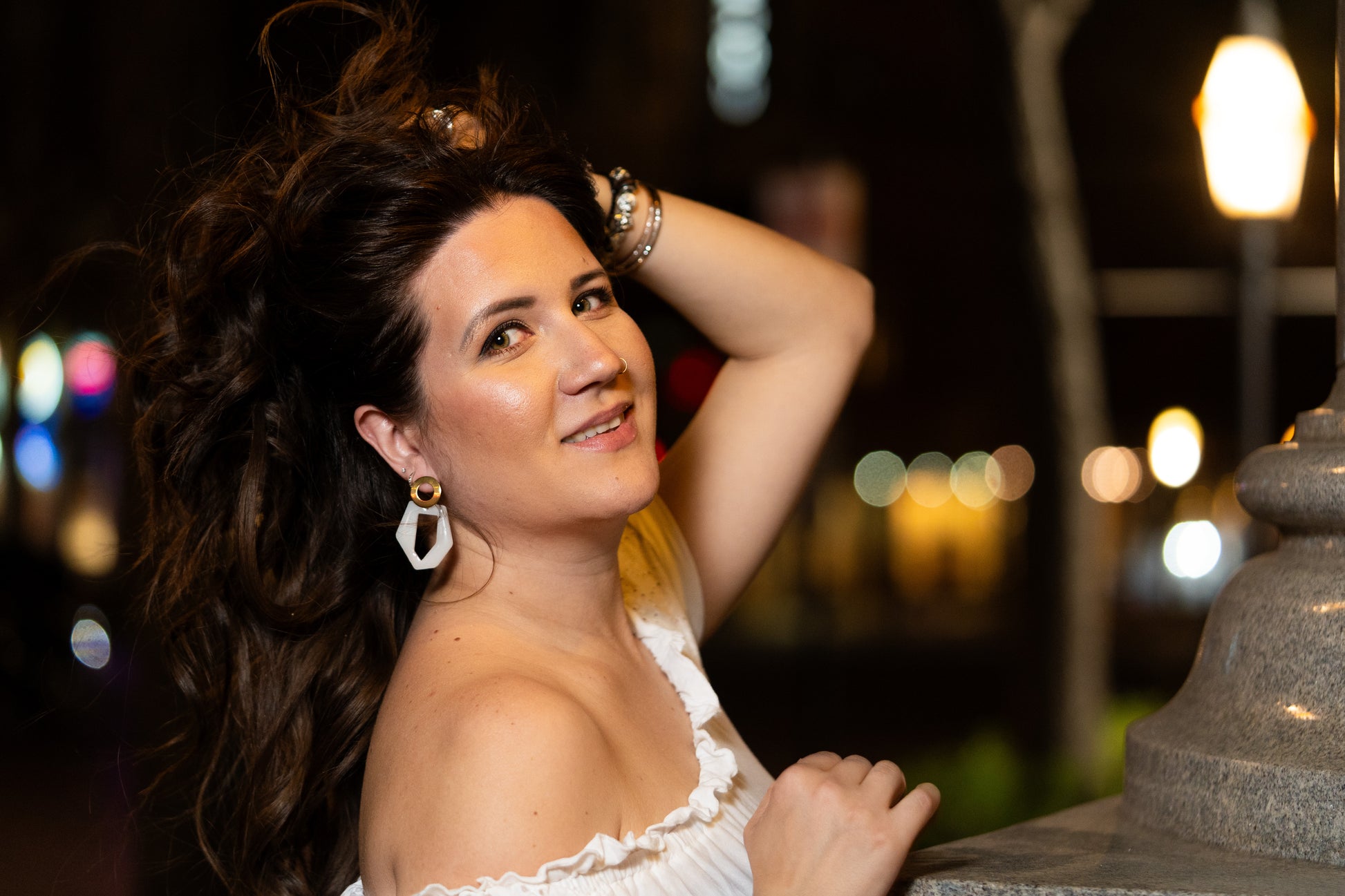 Woman posing outdoors at night with blurred lights in the background wearing Sherami Collection earrings