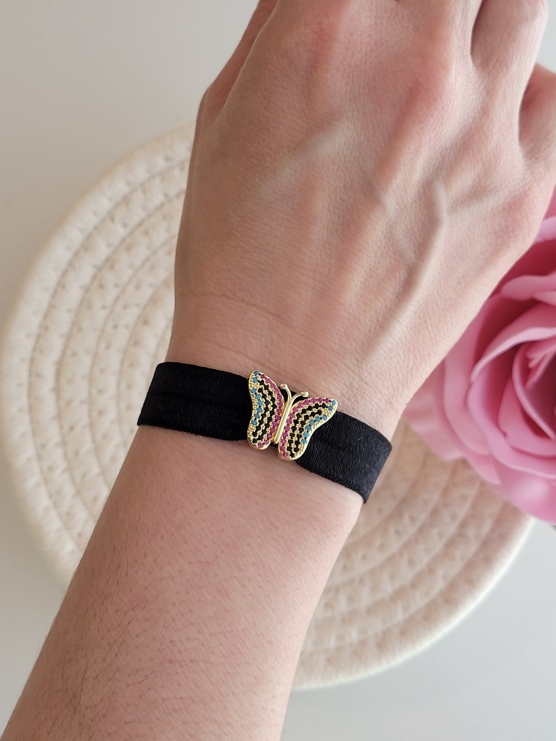 Pulsera elastica negra con mariposa puesta en la muñeca