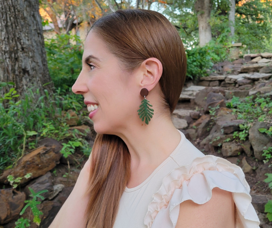 Aretes de hojas verdes tropicales con engache de madera marrón puestos en una modelo.