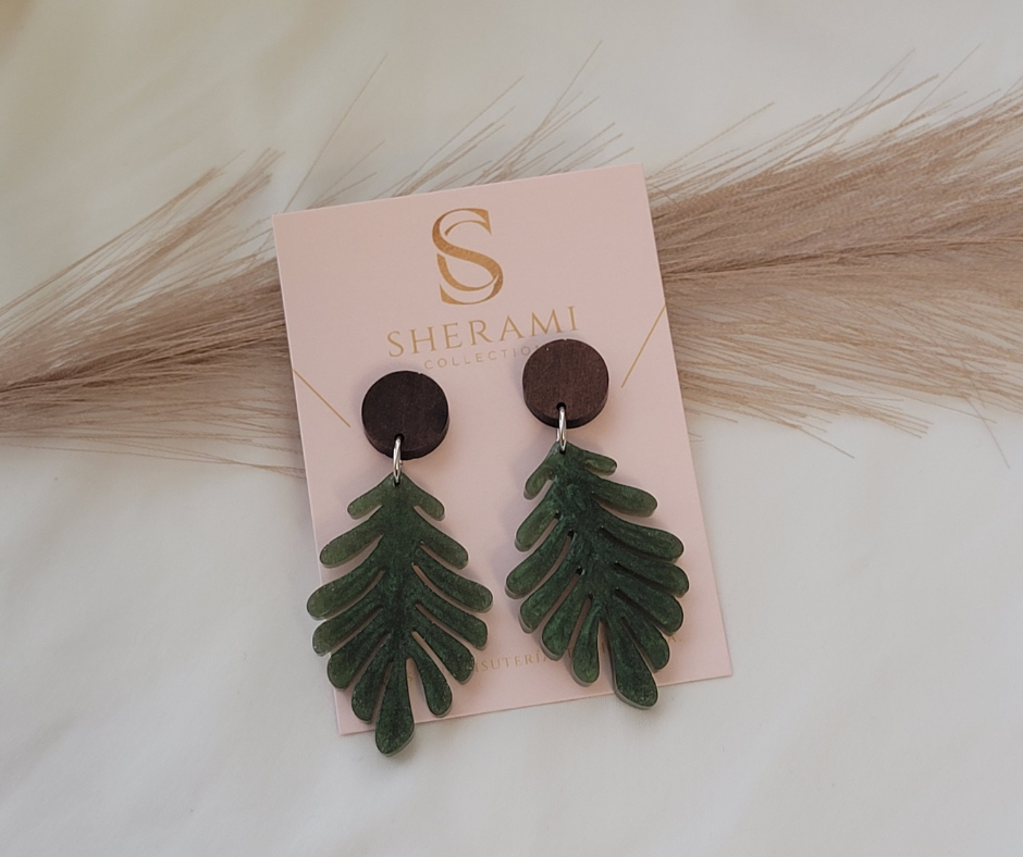 Aretes de hojas verdes tropicales con engache de maddera marrón sobre su tarjeta de display.