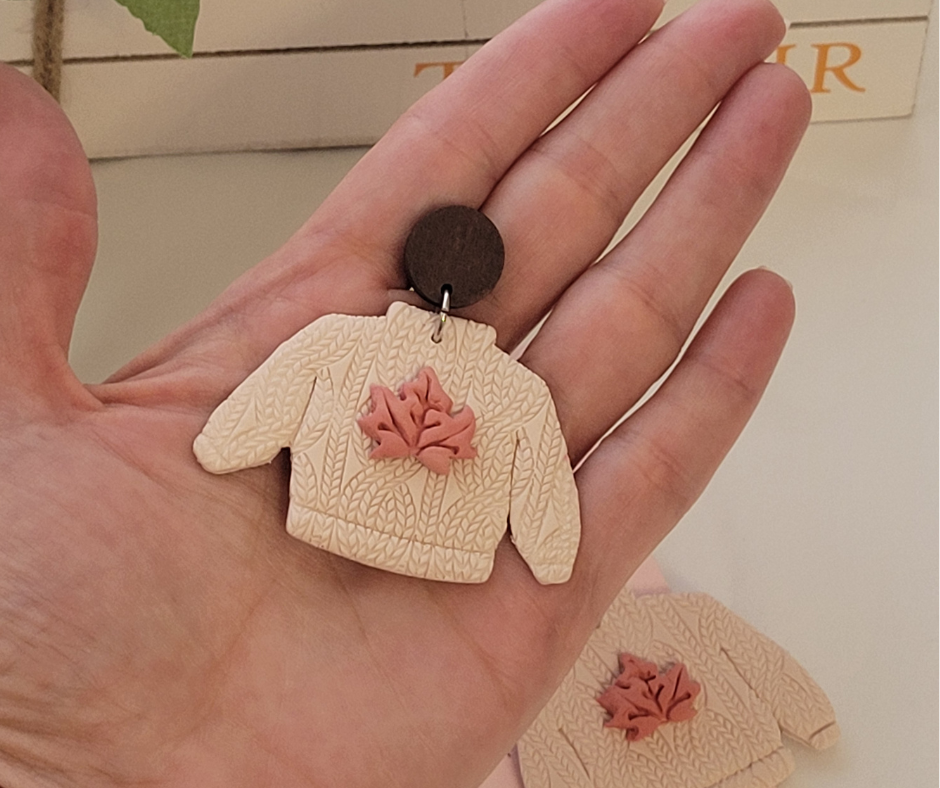 Aretes en forma de sueter sobre una mano para que se pueda apreciar el tamaño